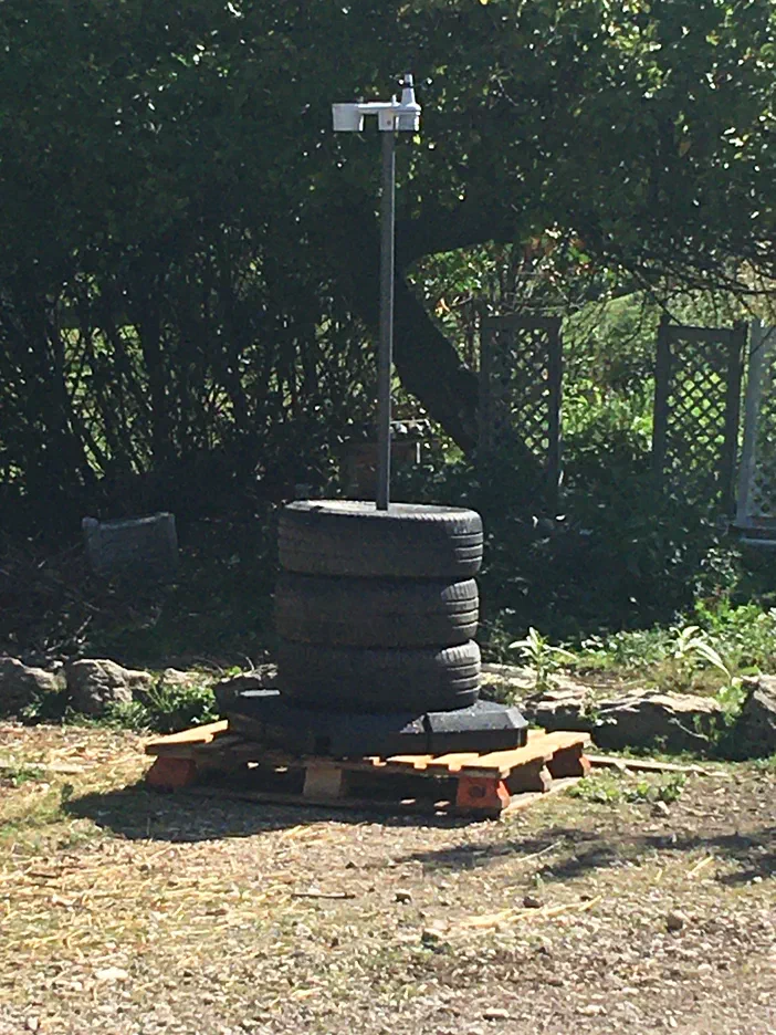 Une station météorologique sur un socle de pneus et une palette, dans un jardin.